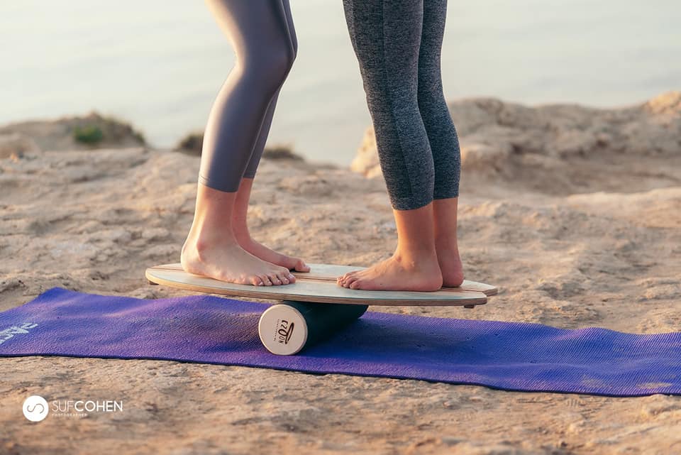 Two people balancing together on a ZoonBoard on the beach